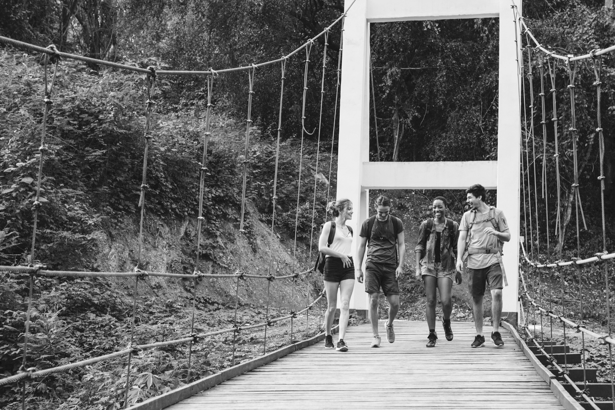 Four friends walking together across a rope bridge